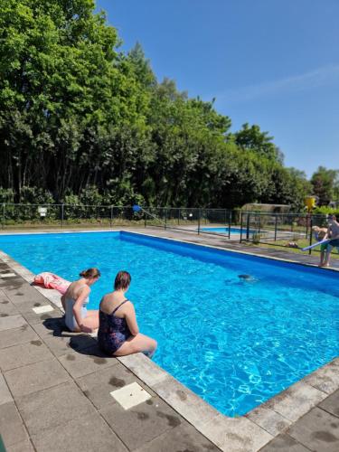 Deux femmes sont assises à côté d'une piscine dans l'établissement Ruime 6 persoons Orlando Super, à De Pol
