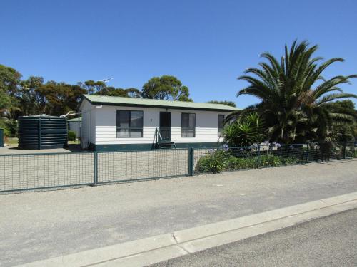 a white house behind a fence on a street at The Shack at Hardwicke in Hardwicke Bay