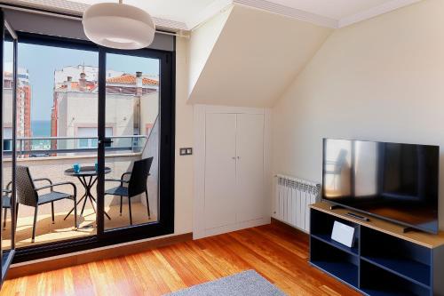 een woonkamer met een tv en een balkon bij Ático con terraza, vistas al mar y parking en playa de S Lorenzo in Gijón