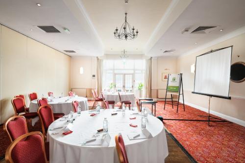 a conference room with white tables and chairs and a screen at Holiday Inn Reading West by IHG in Reading