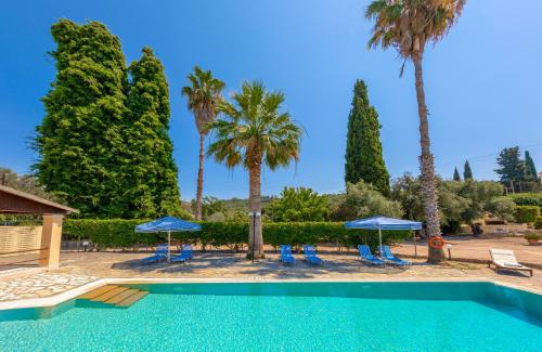 a swimming pool with palm trees and blue umbrellas at Villa Lianolia in Perítheia