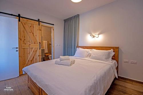 a bedroom with a large white bed with a wooden headboard at הרימון- צימר בוטיק לזוג במעלה גמלא in Ma'ale Gamla