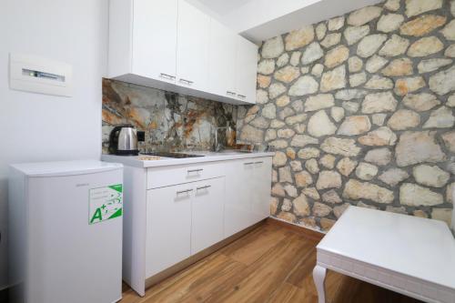 a kitchen with white cabinets and a stone wall at Vila Dena in Vlorë