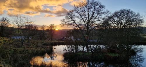 a sunset over a body of water with trees at Canvas & Campfires, Luxury Safari Tent Glamping, only Seren Tent has a hot tub in Lampeter