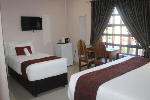 a hotel room with two beds and a desk and a window at Mmathaba Guest House in Mmadinare