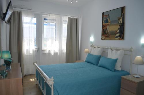 a bedroom with a blue bed with blue sheets and windows at Rania Bella Vista Studios in Poros