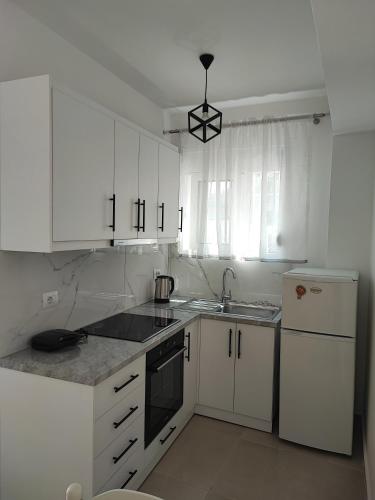 una cucina con mobili bianchi, lavello e frigorifero di Ritas Apartament a Sarandë