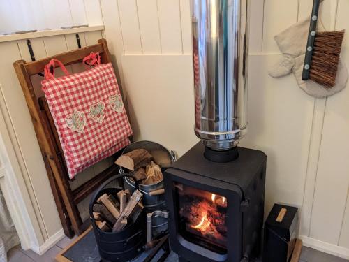 a stove sitting in a room with a fire at Hut In The Glade, Shepherds Hut with Hot Tub in Fryup