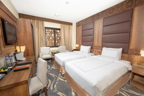 a hotel room with two beds and a desk and a television at Dallah Taibah Hotel in Al Madinah