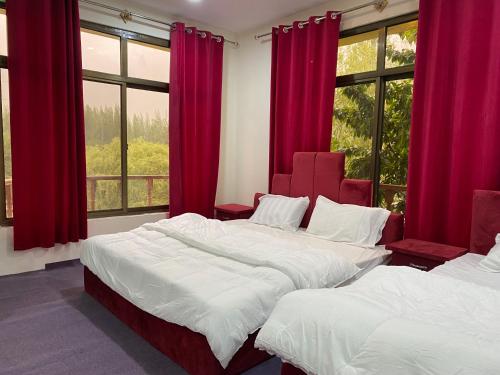 two beds in a room with red curtains and windows at Kamals Lodge in Skardu