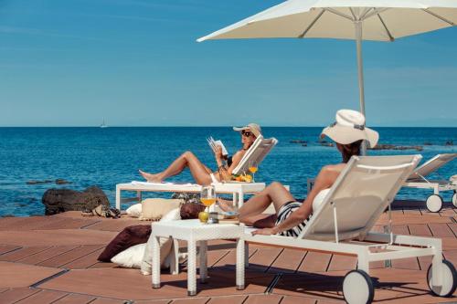 two women sitting on the beach under an umbrella at Apartments Amfora Plava Laguna in Umag