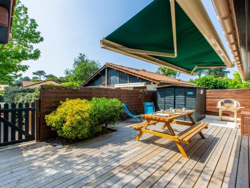 une terrasse en bois avec une table de pique-nique et un parasol vert dans l'établissement Holiday Home Paradise Océan-13 by Interhome, à Capbreton