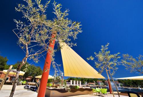 a yellow umbrella and some chairs and trees at Apartments Amfora Plava Laguna in Umag