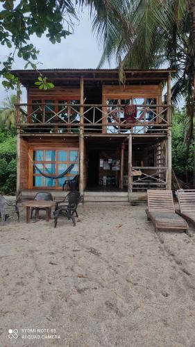 a house on the beach with benches in front of it at HOSTAL Estrellas del tayrona playa in Santa Marta