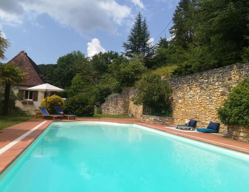une grande piscine avec des chaises et un mur en pierre dans l'établissement Le Baron Perché, à Saint-Cyprien