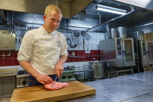 a man cutting up a piece of meat on a cutting board at Kleivstua Hotel near Krokskogen in Sundvollen
