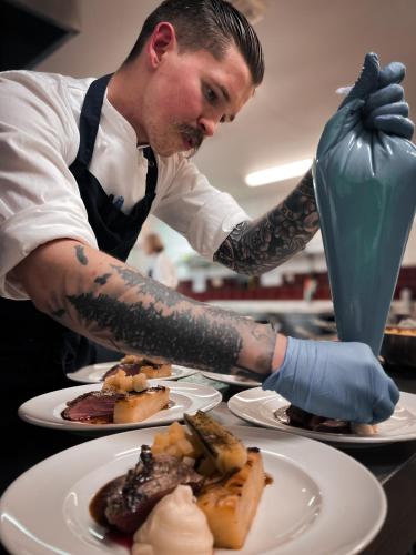 a chef with tattoos on his arms preparing food at Kleivstua Hotel near Krokskogen in Sundvollen