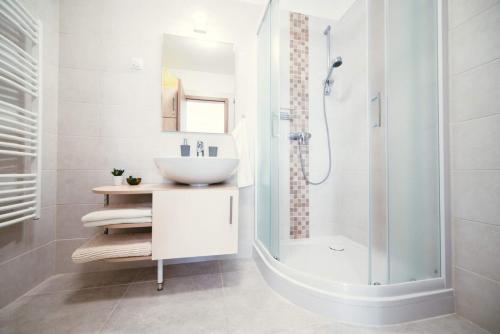 a white bathroom with a sink and a shower at D&B Lelle Apartman in Balatonlelle