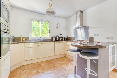 une cuisine avec des armoires blanches et un comptoir avec des tabourets dans l'établissement Les Magnolias Valbonne, à Valbonne