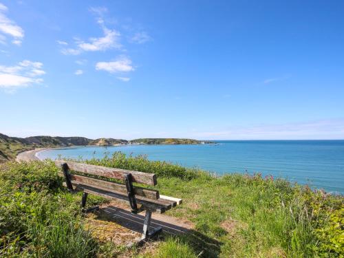 a wooden bench sitting on a hill overlooking the ocean at Tan Parc in Pwllheli