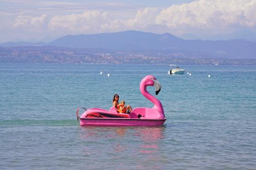 two people riding a pink flamingo boat in the water at San Francesco Camping Village in Desenzano del Garda