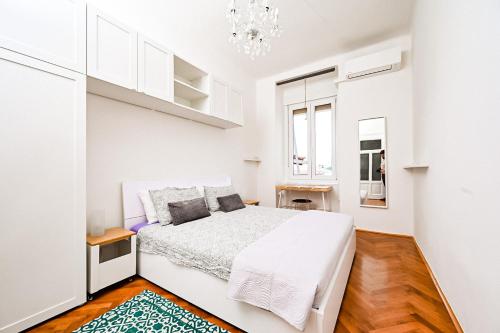 a white bedroom with a bed and a chandelier at '2R' City Center Holidays and Workstays in Rijeka