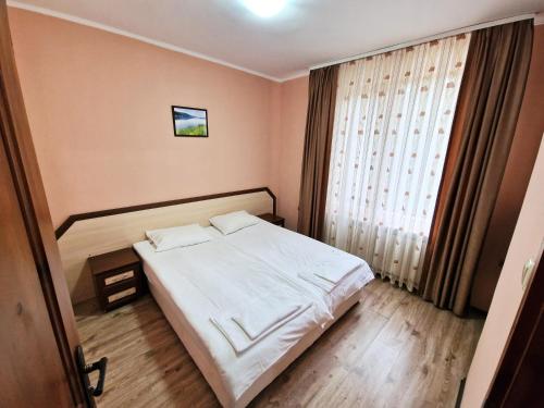 a bedroom with a white bed and a window at Ивелия Къща за гости in Dospat