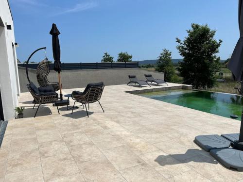 une terrasse avec des chaises, une piscine et un parasol dans l'établissement Villa piscine à débordement, à Pignan