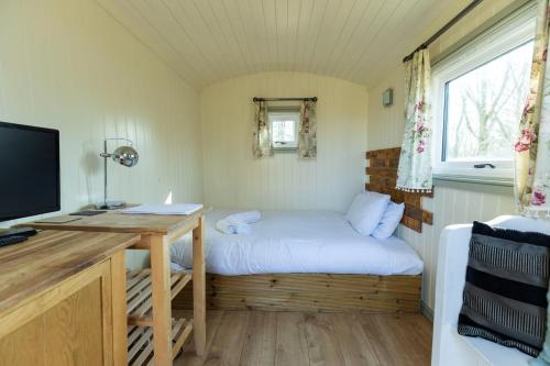 North BradleyにあるFairwood Lakes - Shepherd's Hut with Hot Tubのベッドとデスクが備わる小さな客室です。