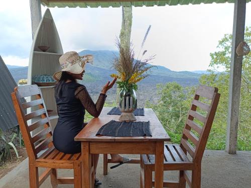 Kintamani Adventure Hidden Lodge في Kintamani: امرأة تجلس على طاولة مع إناء من الزهور