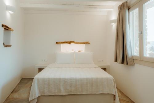 a bedroom with a bed with white sheets and a window at Heliopetra Punta in Ios Chora