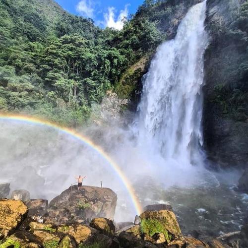 a person standing on a rock near a waterfall with a rainbow at Rainbow Glamping in Abejorral