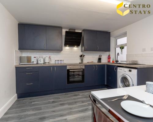 a kitchen with blue cabinets and a washer and dryer at Entire House 3BR 7 Beds Sleeps 8 Ideal for Contractors Families Groups Near Town Centre Hospital Pubs Free Parking WiFi By Centro Stays in Northampton