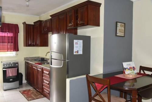 a kitchen with a stainless steel refrigerator and a table at Cozy and Secure Jacaranda Home in Spanish Town