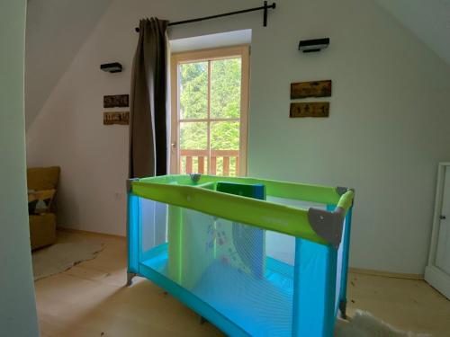 Cuna azul y verde en habitación con ventana en Lovely Cottage in a mountain wilderness of the National Park en Srednja Vas v Bohinju