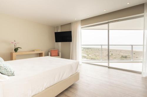 a bedroom with a white bed and a large window at Aqualuz Troia Mar by The Editory in Troia