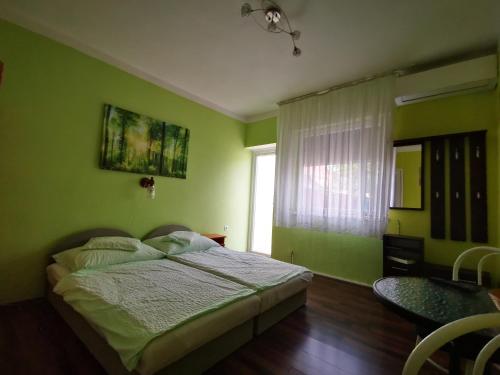 a green bedroom with a bed and a window at Paksy Apartman in Harkány