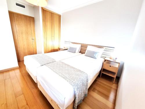 a bedroom with a large white bed and a wooden floor at Casa Pedra da Nau- 2 bedroom APT @Figueira da Foz in Buarcos