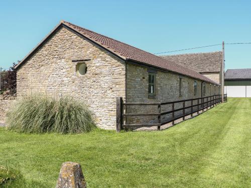 an old brick building with a wooden fence around it at Nutchat Barn in Burford