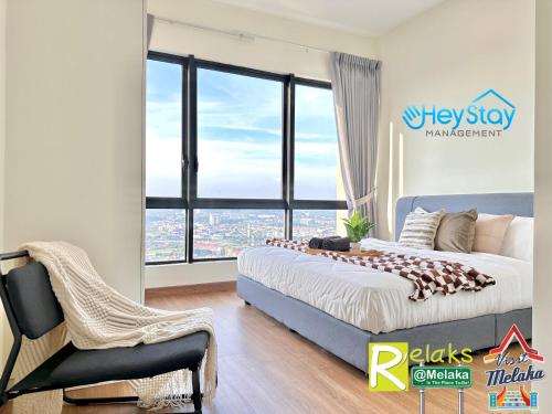 a bedroom with a bed and a chair and a large window at The Apple Residence By Heystay Management in Melaka