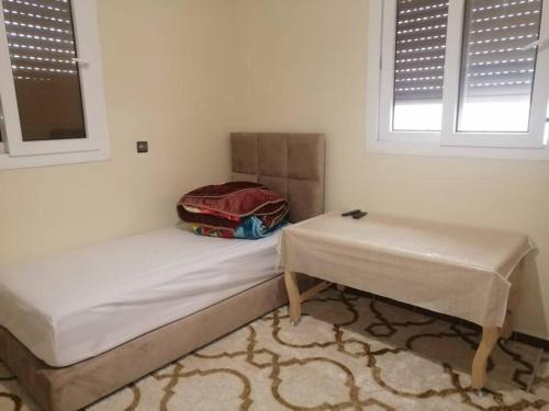 Zimmer mit einem Bett, einem Tisch und 2 Fenstern in der Unterkunft Modern flat Dakhla in Ad-Dakhla
