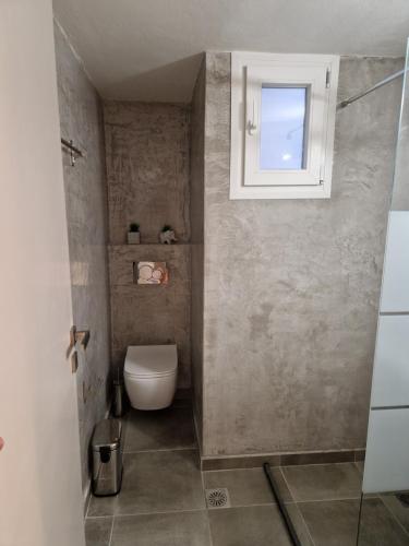 a bathroom with a toilet and a window at Above Apartments near the Airport in Artemida