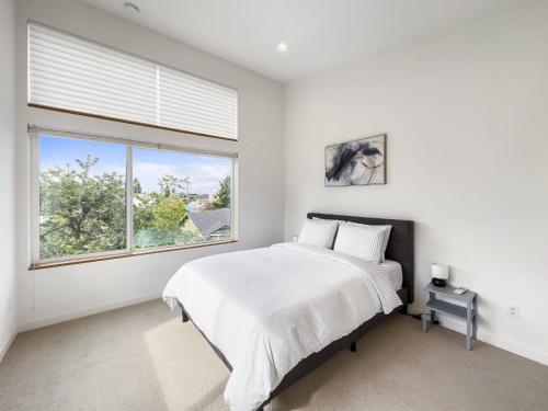 a white bedroom with a bed and a large window at Modern two story townhouse near light rail in Seattle