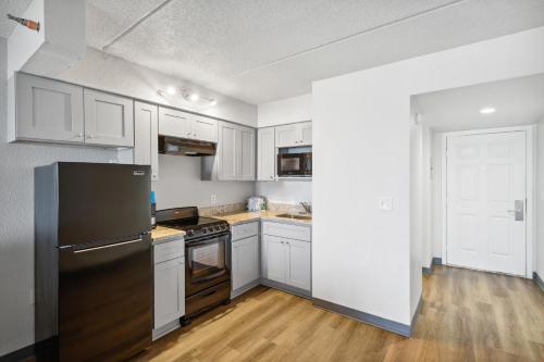 a kitchen with white cabinets and a black refrigerator at Sugar Sands Beachfront Hotel, a By The Sea Resort in Panama City Beach