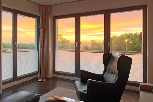 a living room with a chair and windows with the sunset at Villa Deichgraf 12 "Meerblick" in Börgerende-Rethwisch