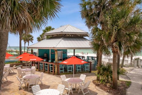 un restaurante de playa con mesas, sillas y palmeras en Beachcomber Beachfront Hotel, a By The Sea Resort, en Panama City Beach