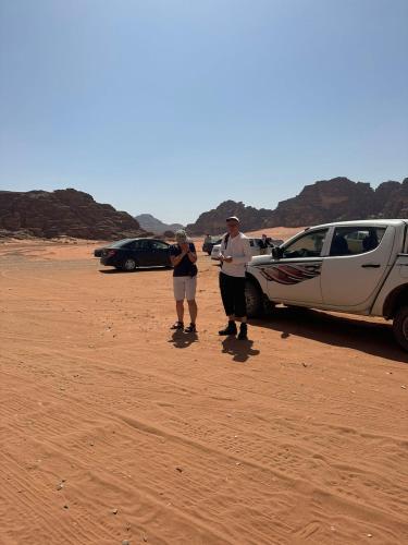 two people standing next to a car in the desert at Yara camp in Wadi Rum