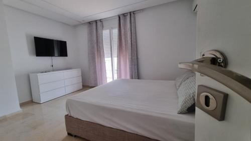 a white bedroom with a bed and a television at Le 6éme in Sousse
