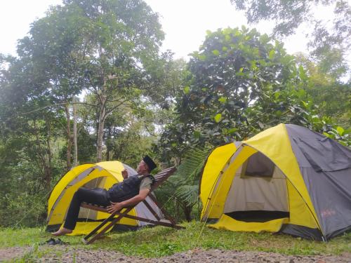 a man sitting on a chair in between two tents at Joben Ecolodge in Tetebatu