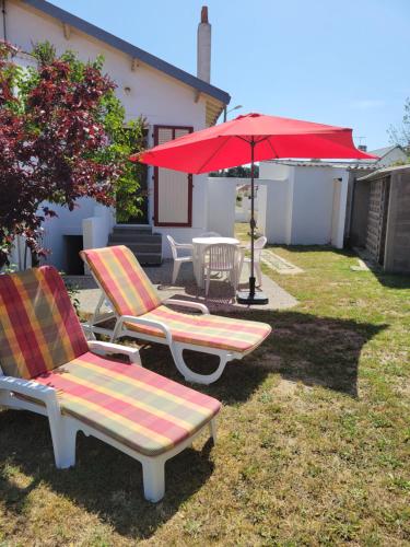 two chairs and a red umbrella in a yard at EOLE - Maison Saint Jean de Monts - 2 pièces - 4 personnes in Saint-Jean-de-Monts